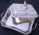 A William IV sterling silver entree dish and cover with armorial finial on electroplate two handled stand